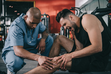 a man holding his knee in pain with a medical professional checking his knee with his hand